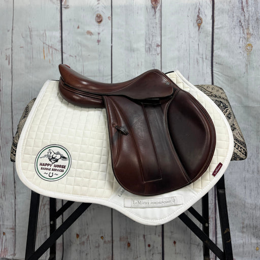 Brown leather saddle on a white saddle pad with a visible brand logo against a wooden background